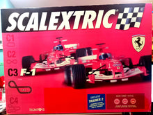 Carregar imagem no visualizador da galeria,  Circuito de Scalextric con 2 coches F1 Ferrari F2004. El circuito tiene forma de 8 prolongado con unas dimensiones de 2.93 m x 1.38 m y un total de 6.49 m de recorrido. El estuche incluye un trainer 2 para poder competir contra la máquina cuando sólo un hay 1 corredor 